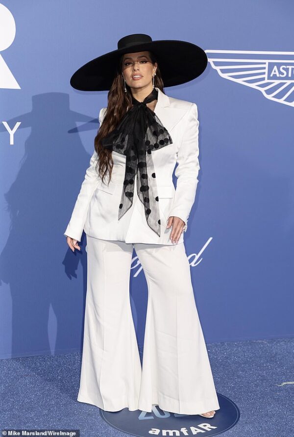 Ashley Graham turns heads in an enormous wide-brimmed hat and flares at the amfAR Cannes Gala